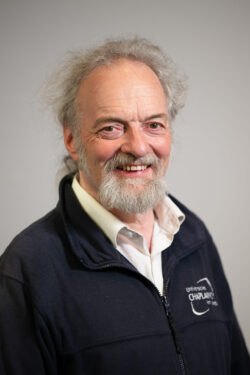 Robin has long silver grey hair tied back with a short beard and moustache. 